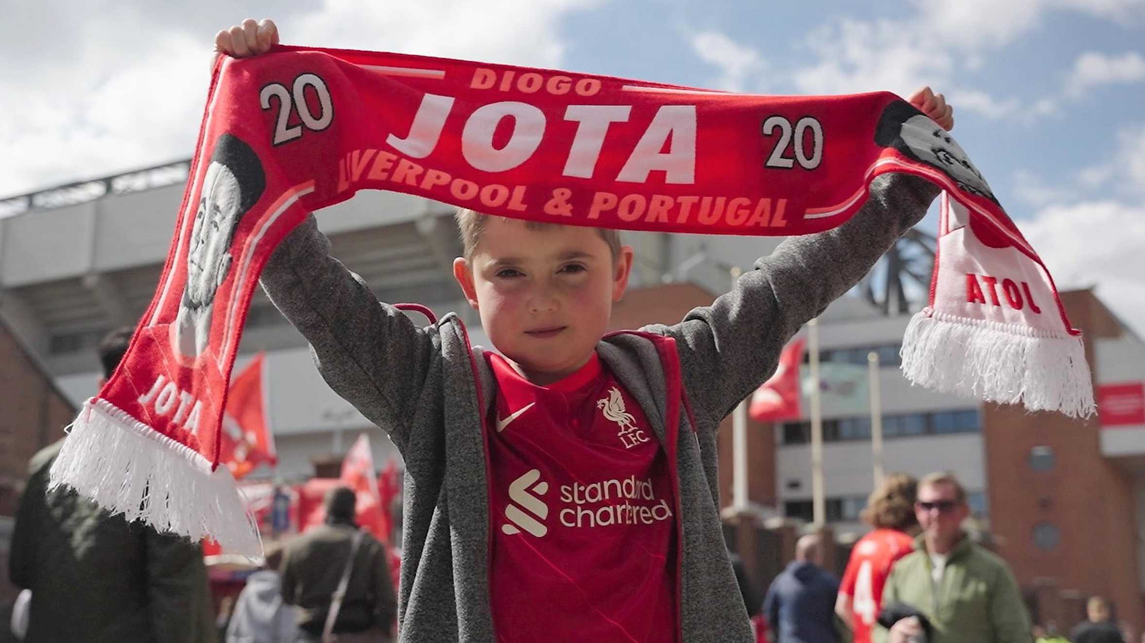 Archie holding up a Liverpool FC scarf outside Anfield Stadium.