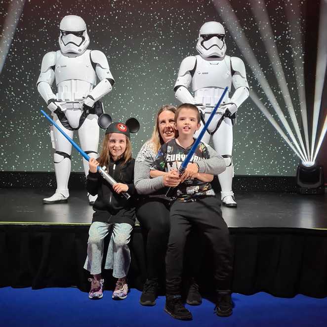 Lewis, mum and Lily-Grace holding light sabres, with two Stormtroopers in the background.